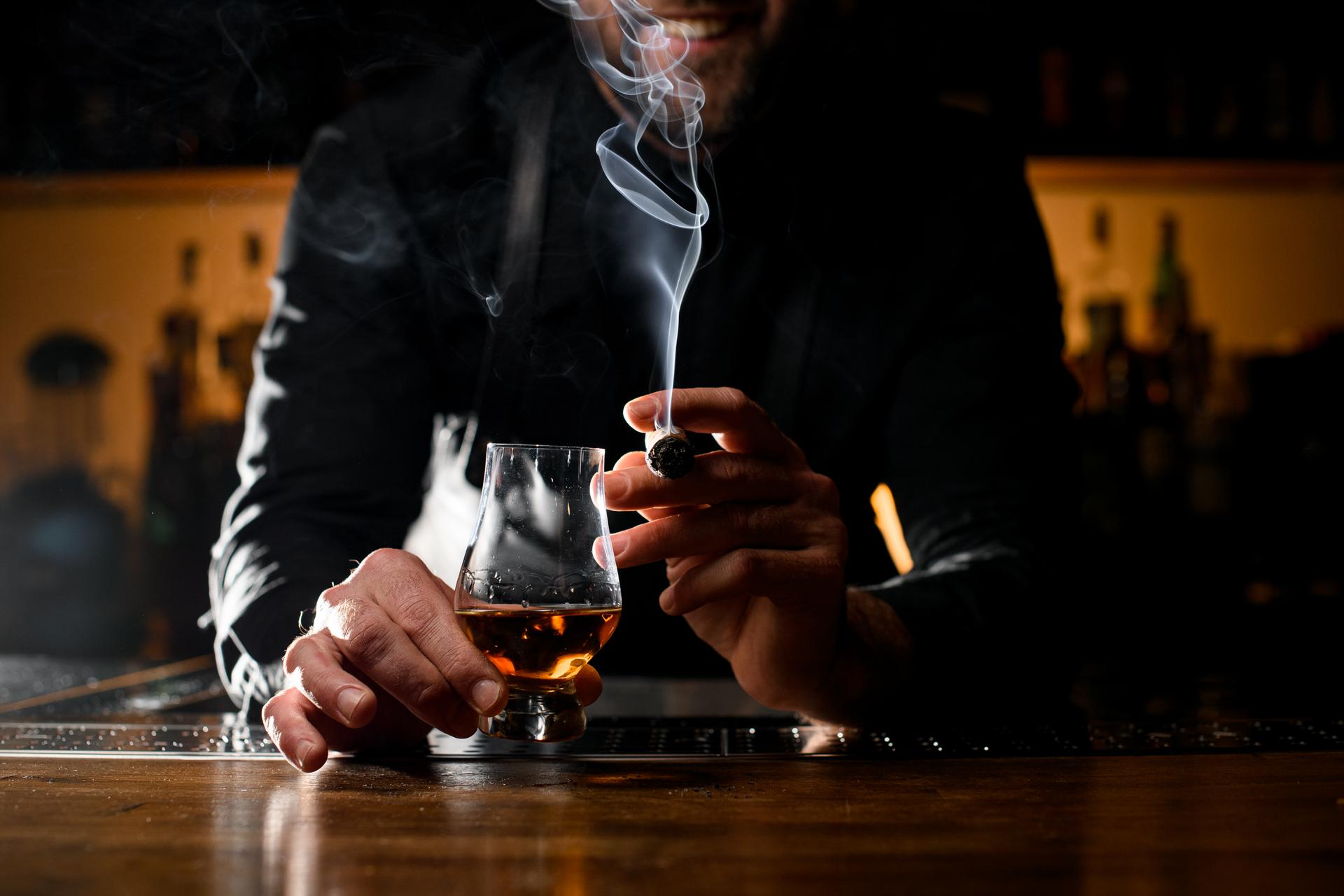 beautiful view of male hands holding a glass of alcoholic drink and smoking cigar