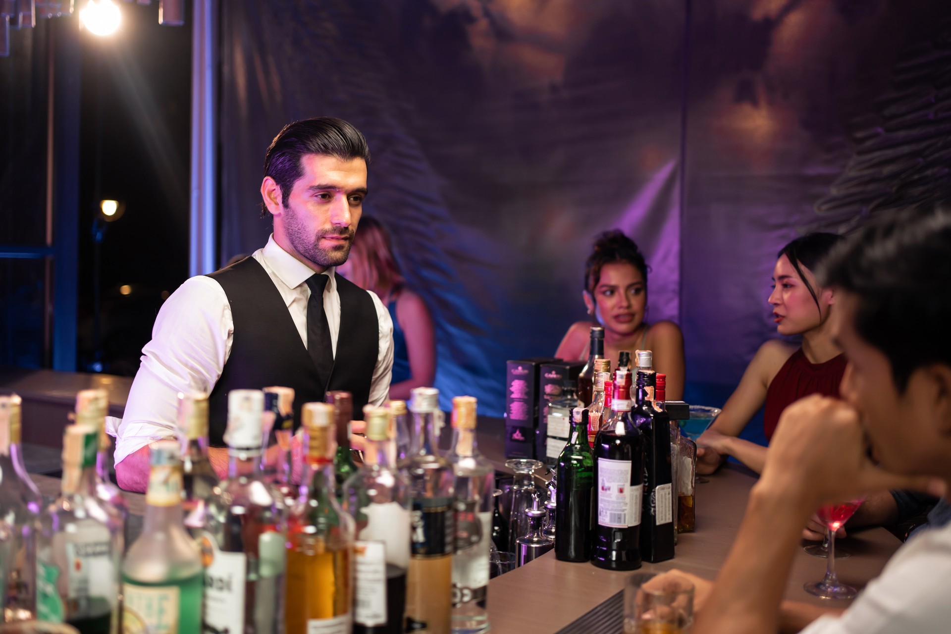 Caucasian profession bartender making a cocktail for customer at a bar. Attractive man pouring mixes liquor ingredients cocktail drink from cocktail shaker into the glass at night club restaurant.